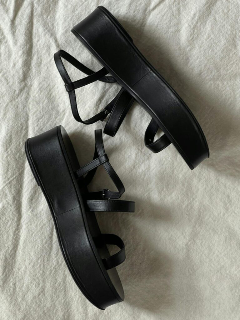 Stylish black platform sandals with straps, displaying modern fashion on white fabric.