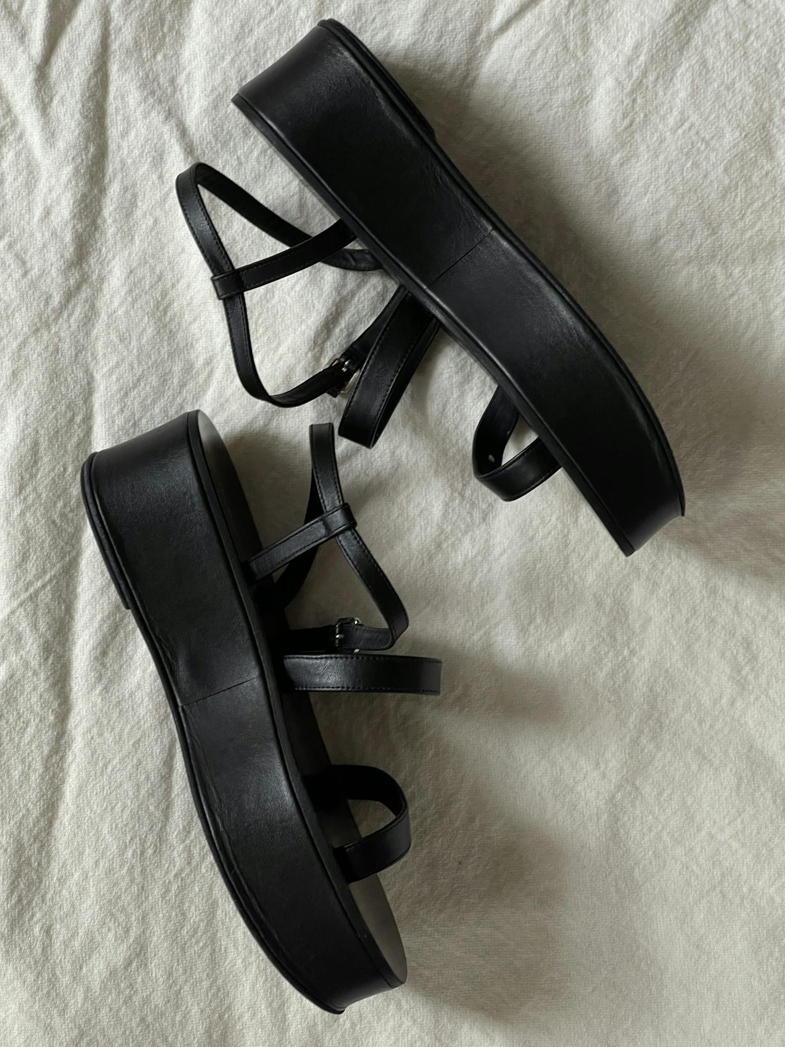 Stylish black platform sandals with straps, displaying modern fashion on white fabric.